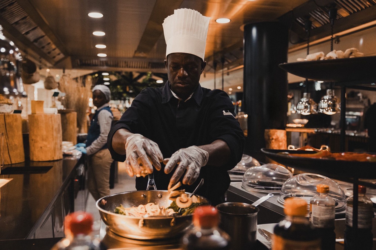 A cook putting ingredients in a pan.