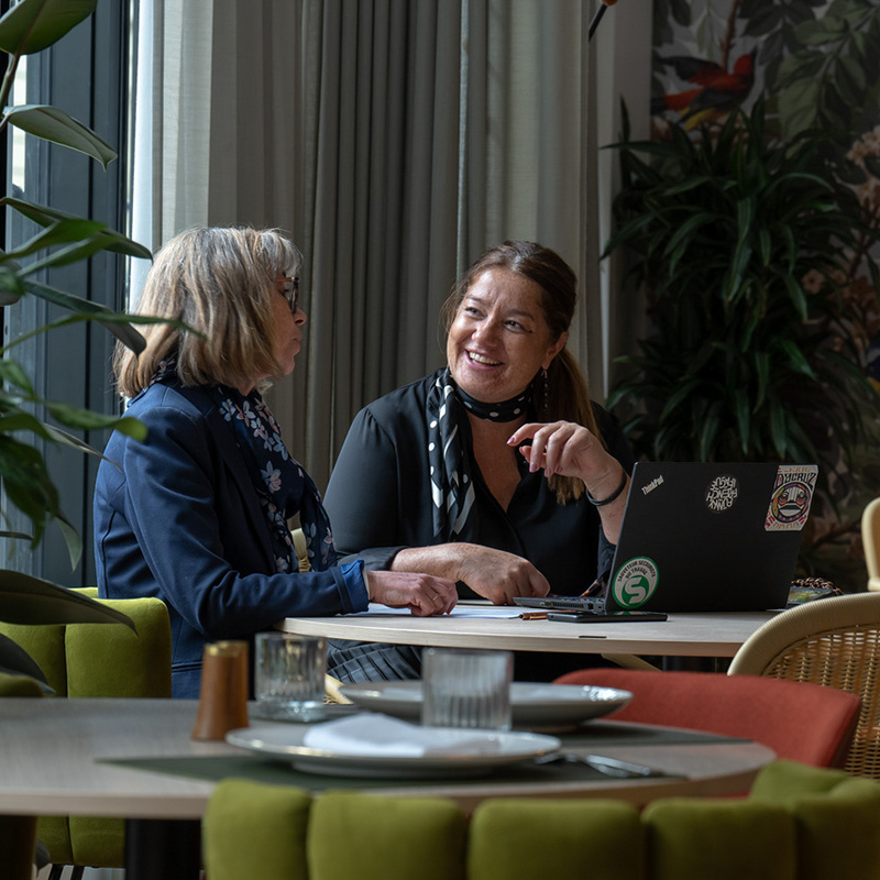 Two women discussing work at a casual table setup.