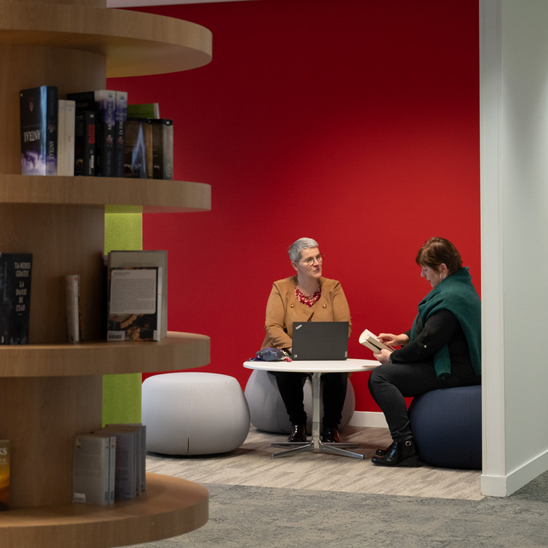 Two women chatting in modern office corner.