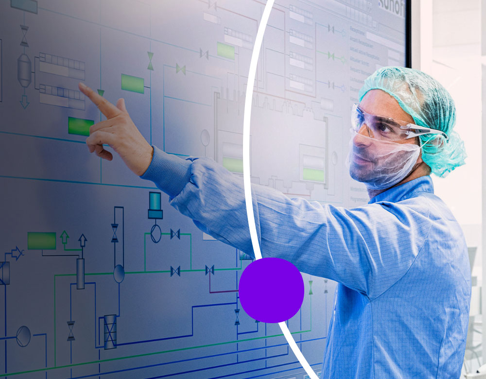 A man dressed in lab scrubs pointing to a technical diagram with a man and a woman watching.