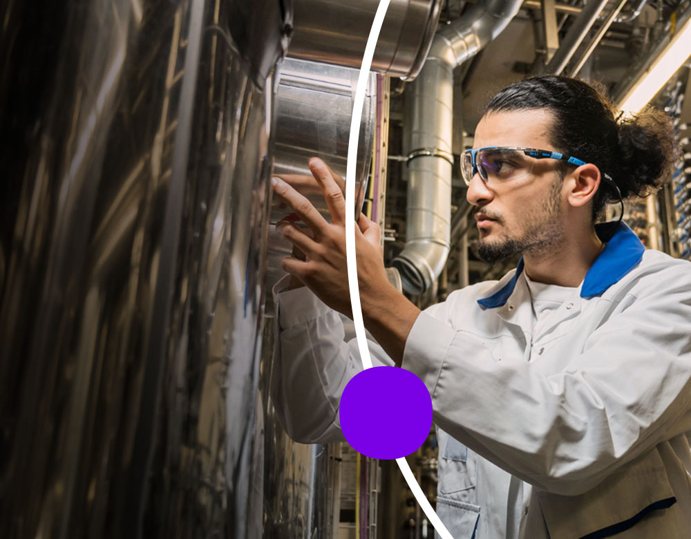 A lab worker observes a large silver tank.