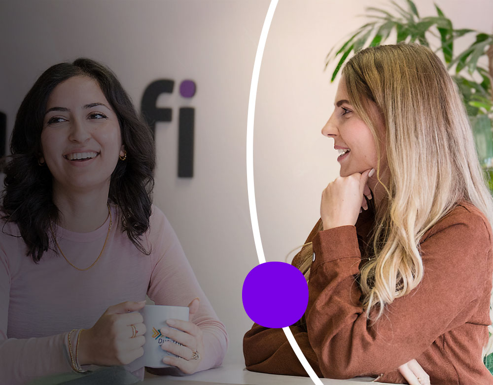 Two women smiling and talking over coffee in an office.