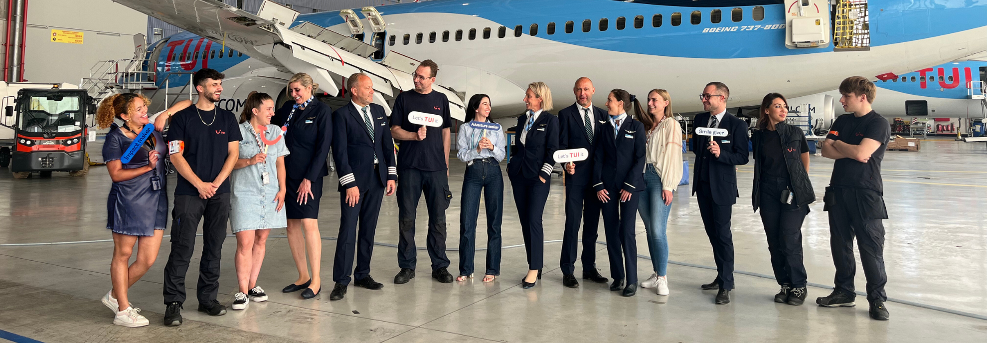 Eine Gruppe von Mitarbeitenden der TUI Fluggesellschaft in marineblauen Uniformen feiert gemeinsam auf einer Terrasse im Freien.