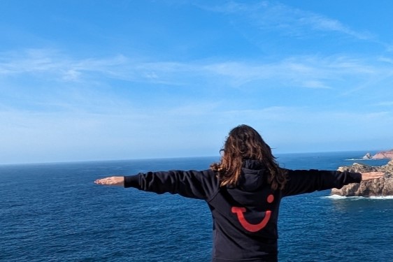 TUI colleague standing on a cliff with open arms in a TUI hoodie