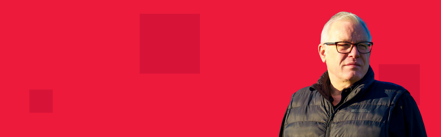 Red background with dark red pixels on top, with a man in a dark gilet and glasses looking towards the camera