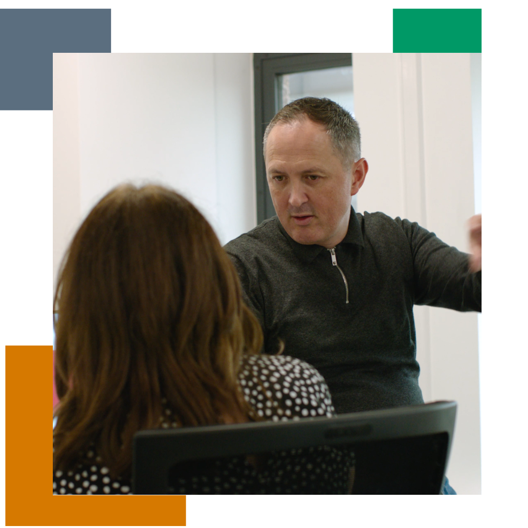 Man talking to a woman in an office, by a work station