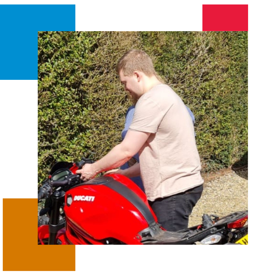 Man in pink t-shirt standing by a Ducati motorbike