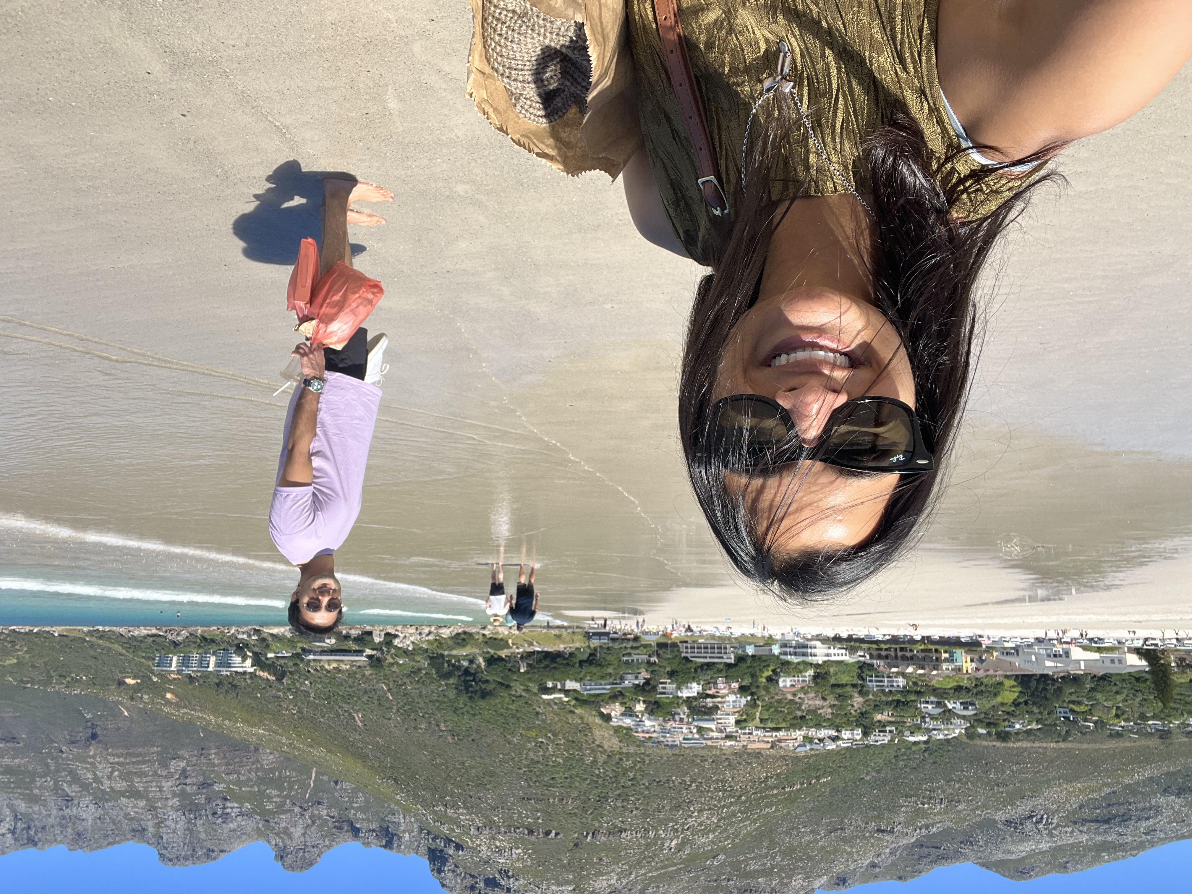 Lady on the beach taking a selfie with a man in the background by the sea