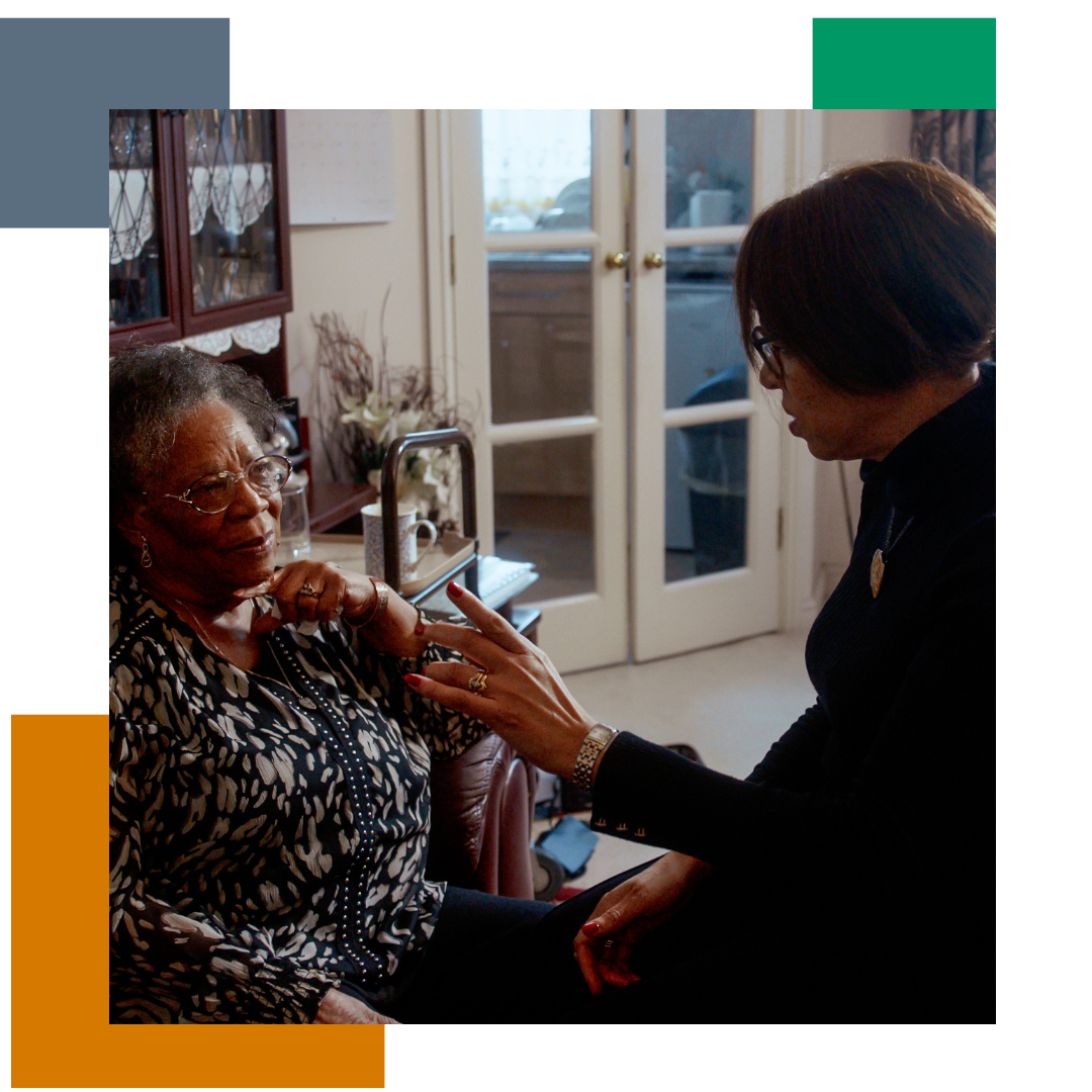 Woman in a home talking to another, older woman, wearing a flowery top