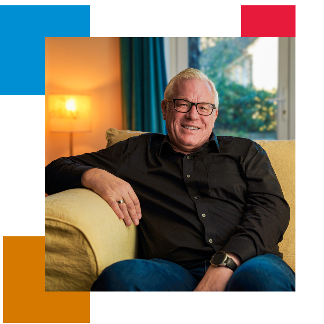 Coloured squares in the background with the main picture being a man in a dark shirt and glasses sat on his sofa, smiling