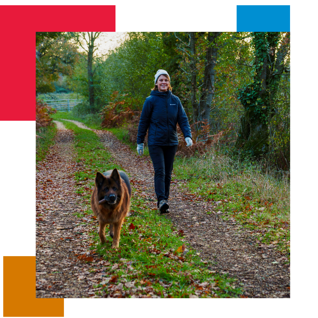 Woman in winter clothing walking her German Shepherd in a woodland path with grass and trees