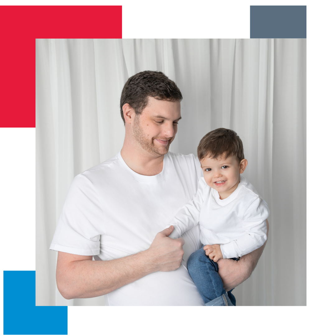 Man with white t-shirt holding child and smiling with a curtain in the background