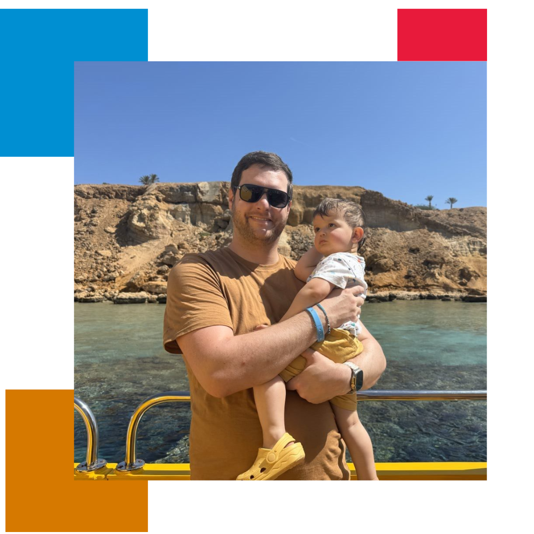 Man holding child and looking at camera smiling with the sea and an island in the background