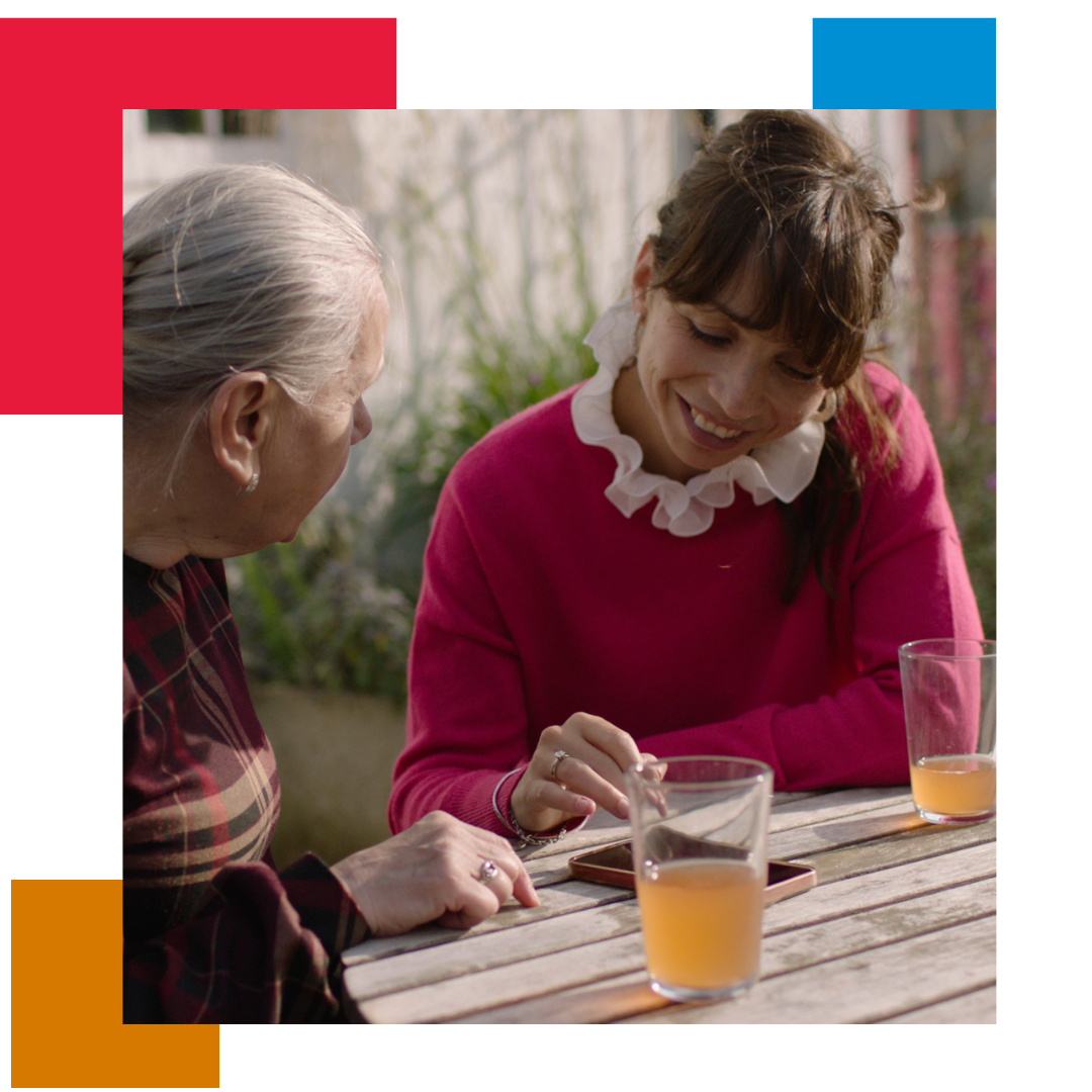 Two women at a table outside with drinks, talking and looking at images on a mobile phone