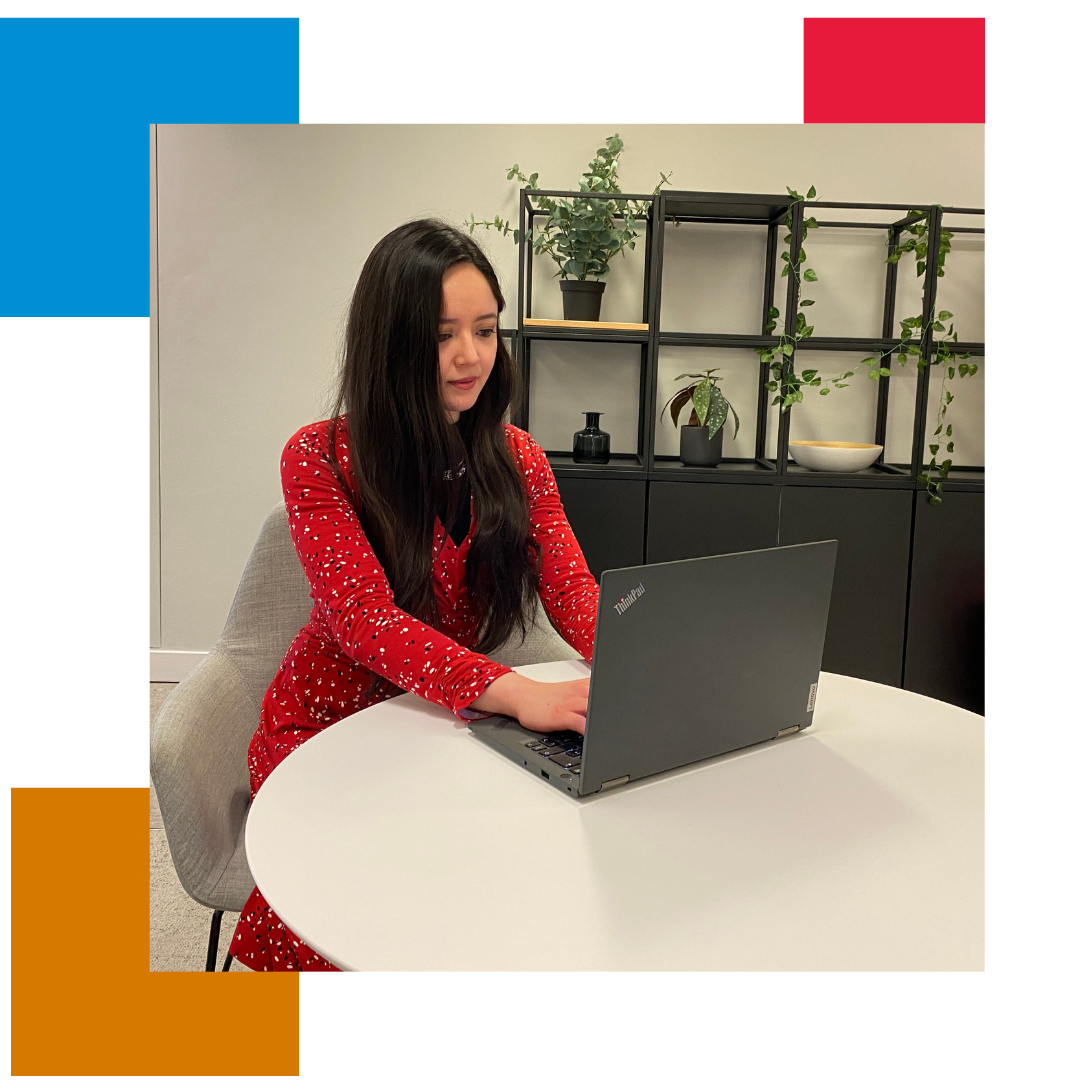 Woman in a red dress sat at a table with her laptop in front of her