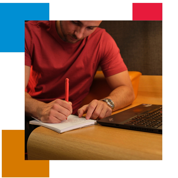 Person writing in notebook beside laptop