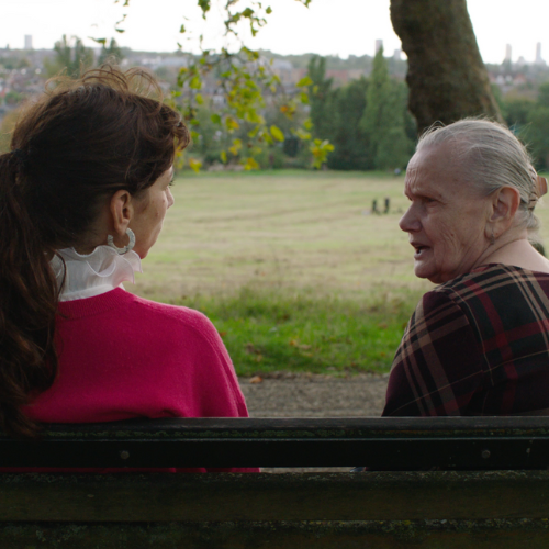 Two women sat on a park bench talking to each other