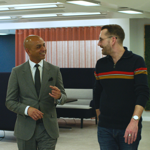 Two men in an office walking through a corridor laughing and chatting