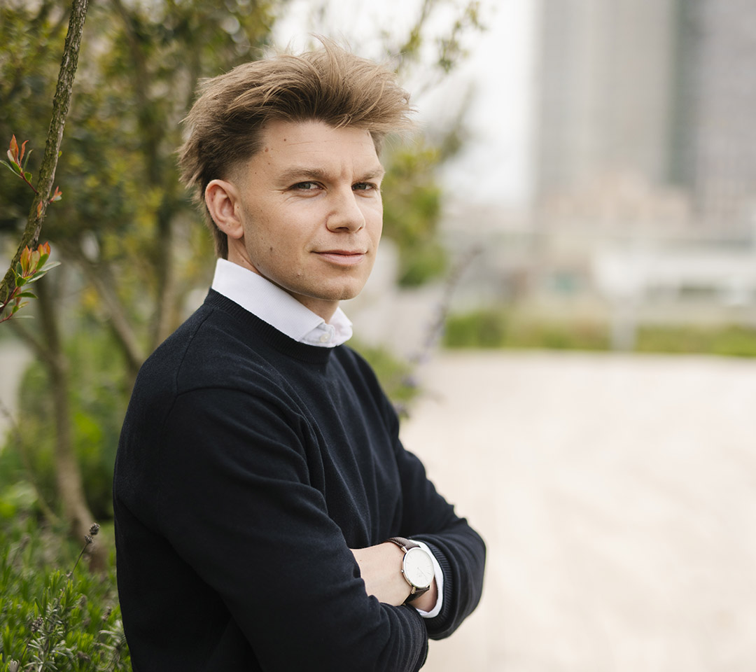 Gilles has blond hair and is wearing a black jumper