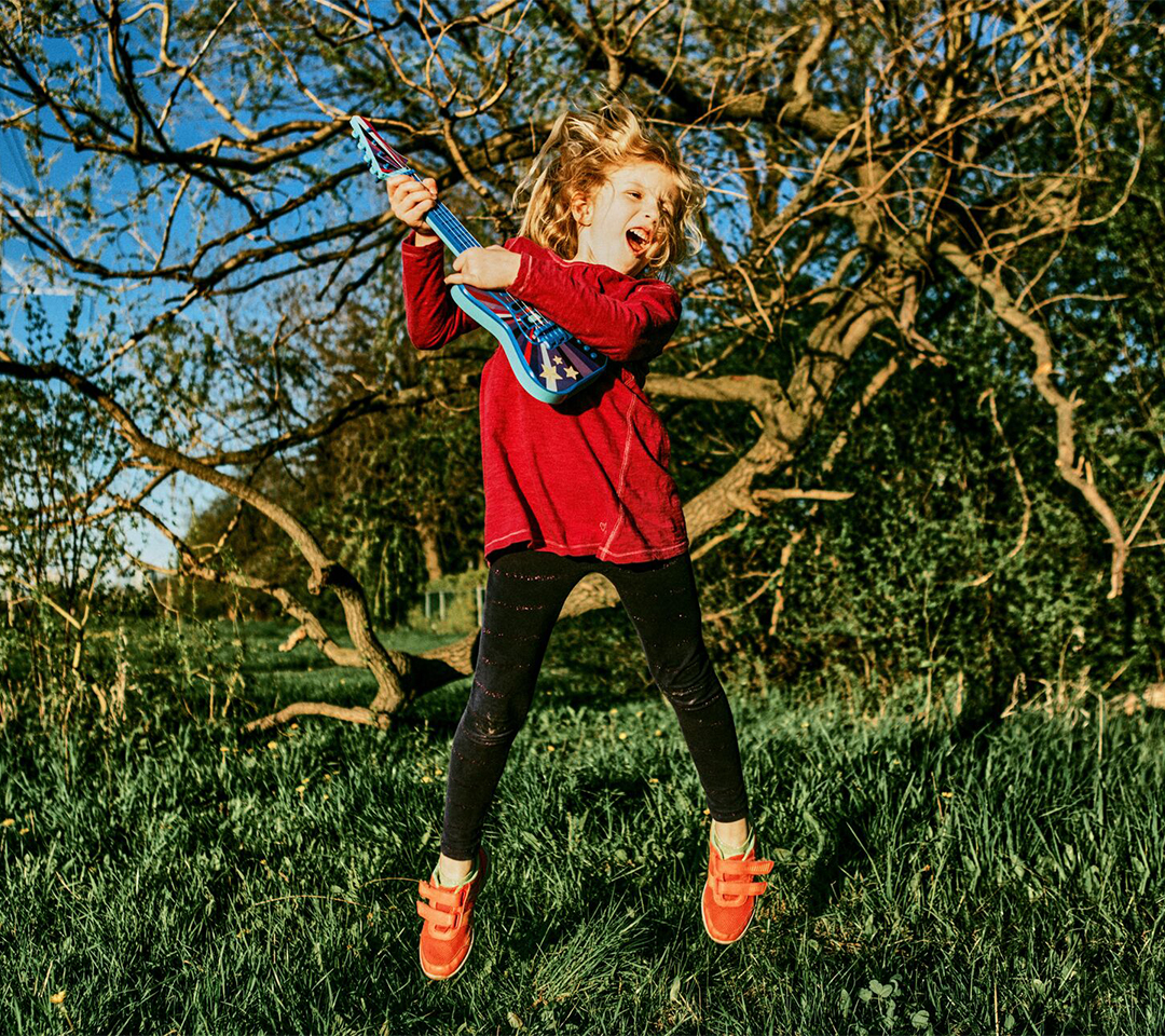 young girl jumping and playing the guitar