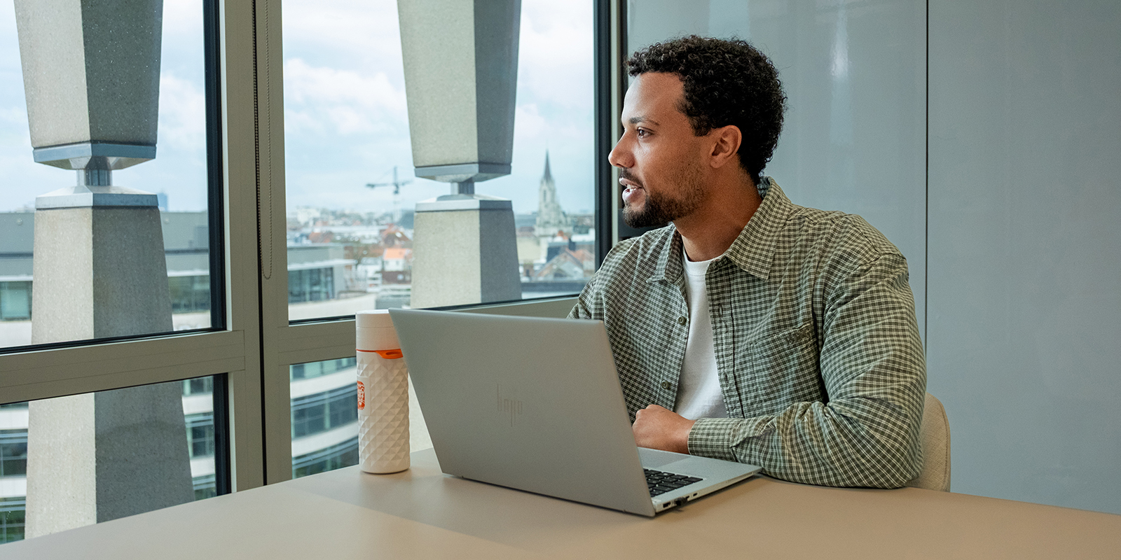 Malik, in front of his laptop, is looking at the window.