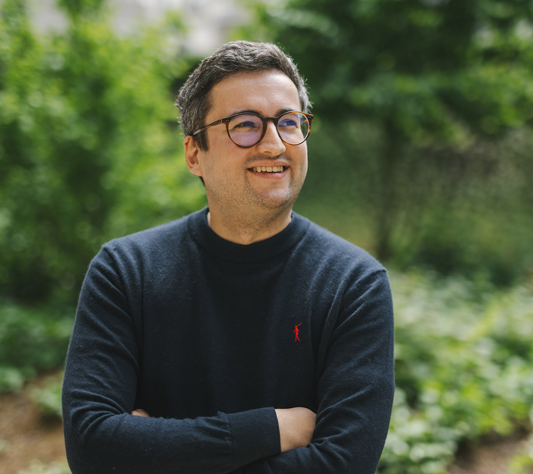 Maxime is wearing glasses and standing in front of trees.