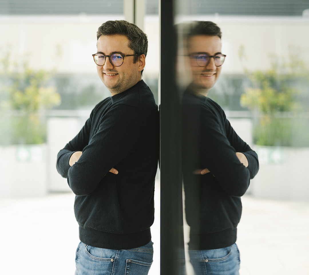 Maxime is leaning on a glass window. His reflection shows.
