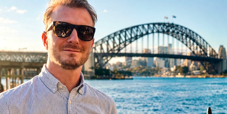 Matthieu is wearing sunglassees and standing in front of a bridge in Sidney