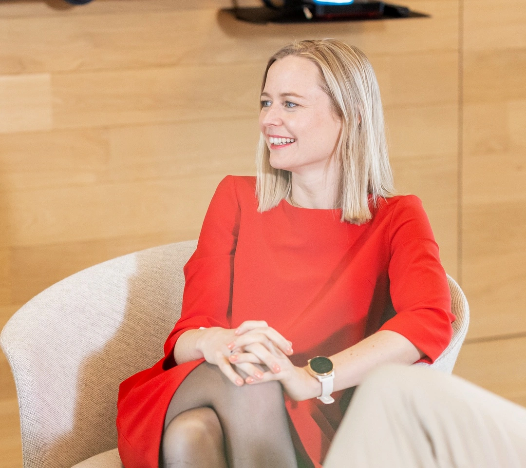 A private banker in a red dress, Laia, is sitting and smiling.