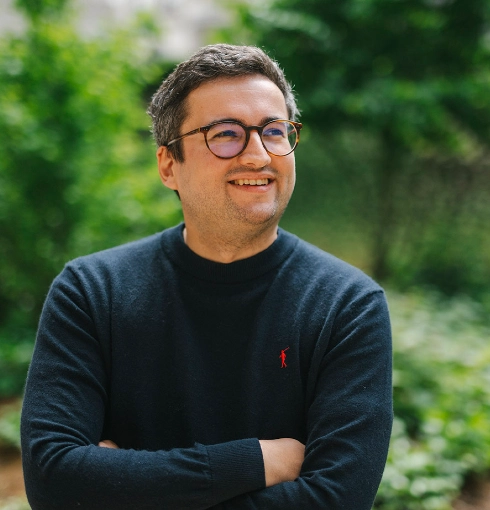 Maxime is wearing glasses and standing in front of trees.