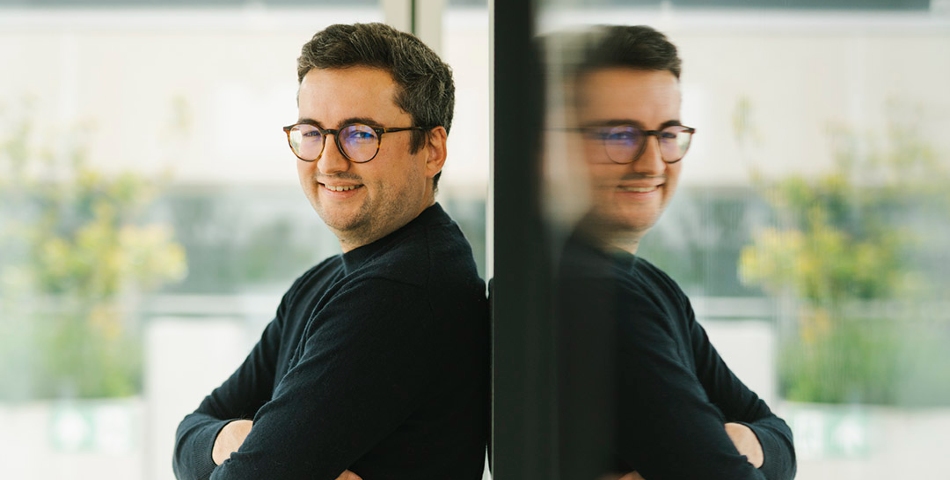 Maxime is leaning on a glass window. His reflection shows.