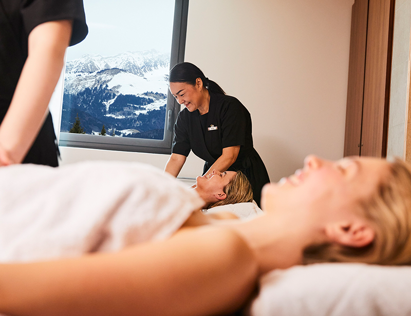 Two clients are receiving massages from two G.O.s, while a window on the wall provides a view of the snowy mountains.