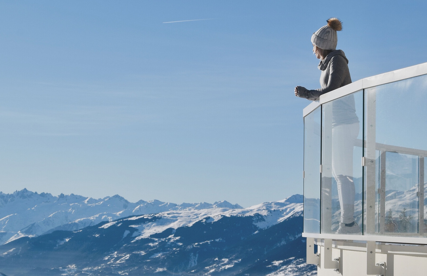 Une jeune femme sur un balcon surplombant les montagnes enneigées des Alpes Françaises dans l'un de nos Resorts