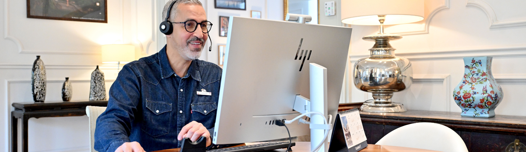 Employee wearing a headset and working on a computer during a remote meeting or customer interaction from an office workspace.