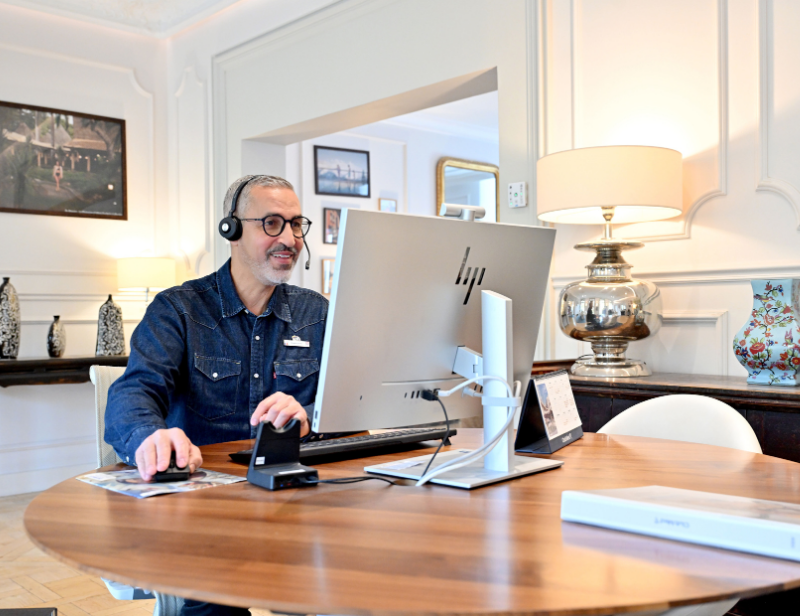 Employee wearing a headset and working on a computer during a remote meeting or customer interaction from an office workspace.