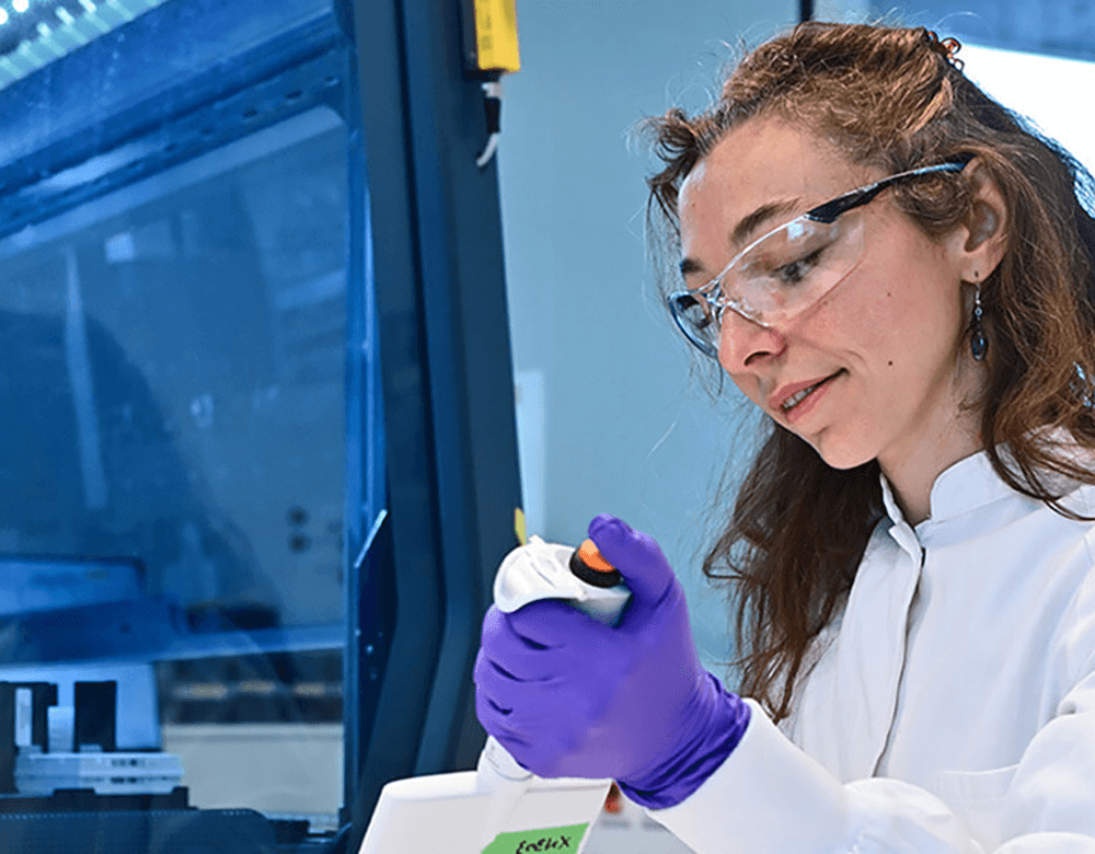 Une femme en blouse et lunettes utilise une pipette pour distribuer un échantillon