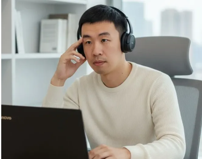 一位戴着耳机的人正在办公桌前使用笔记本电脑。