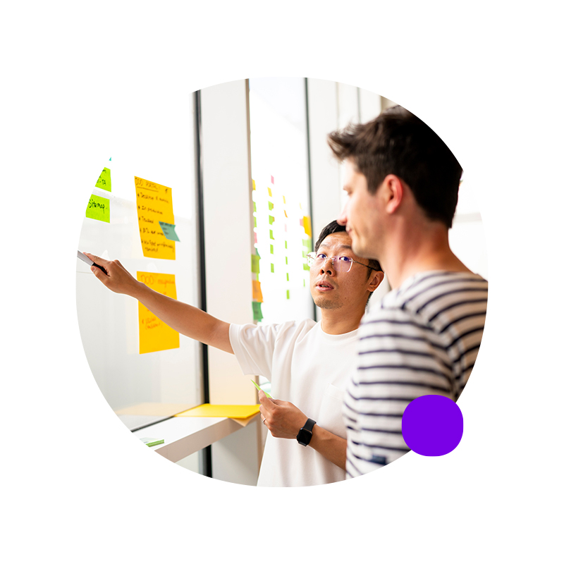 Man at whiteboard pointing to presentation and looking at coworker