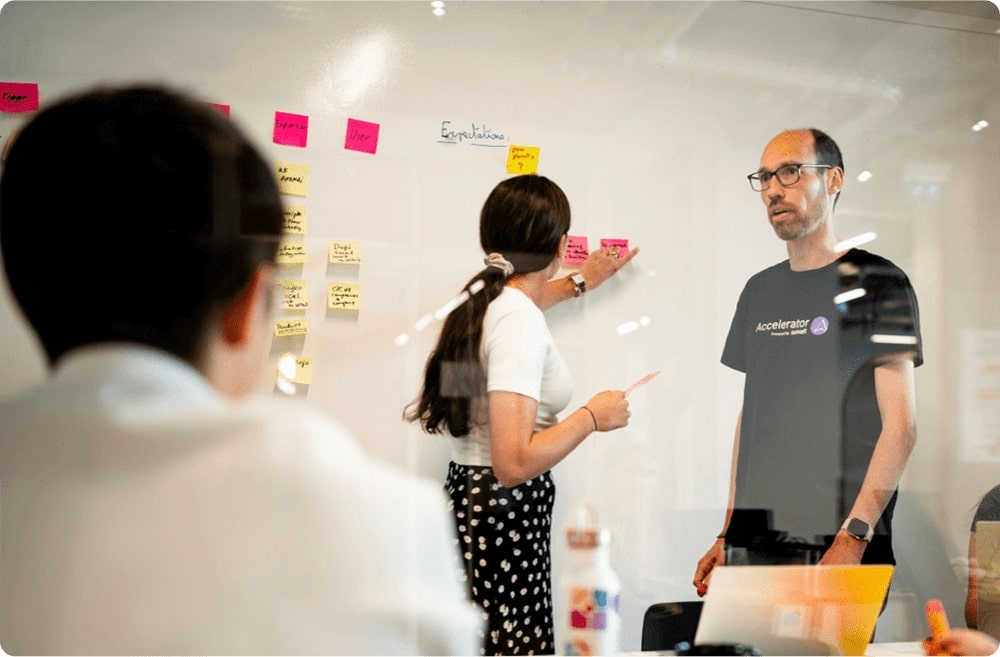 Des gens en conversation devant un tableau blanc rempli de post-it