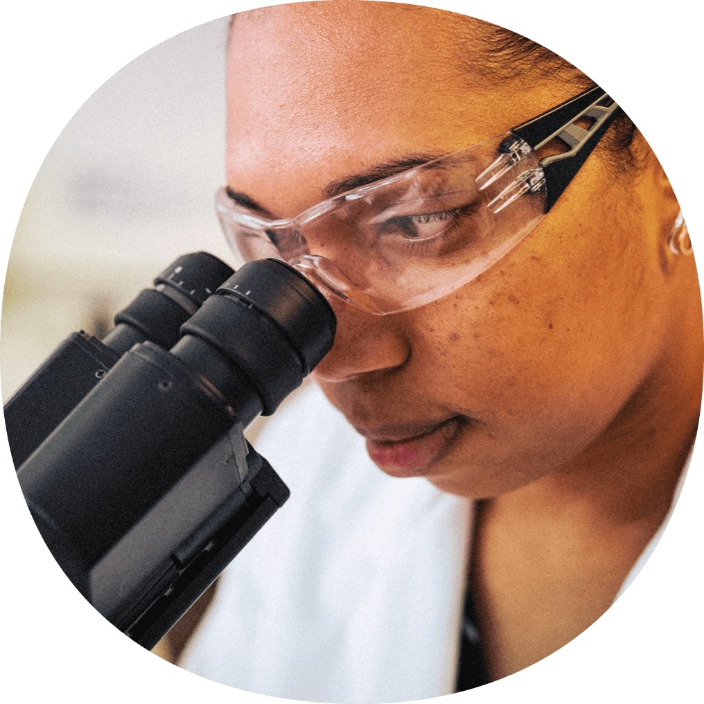 Femme en blouse de laboratoire et lunettes de sécurité regardant un microscope