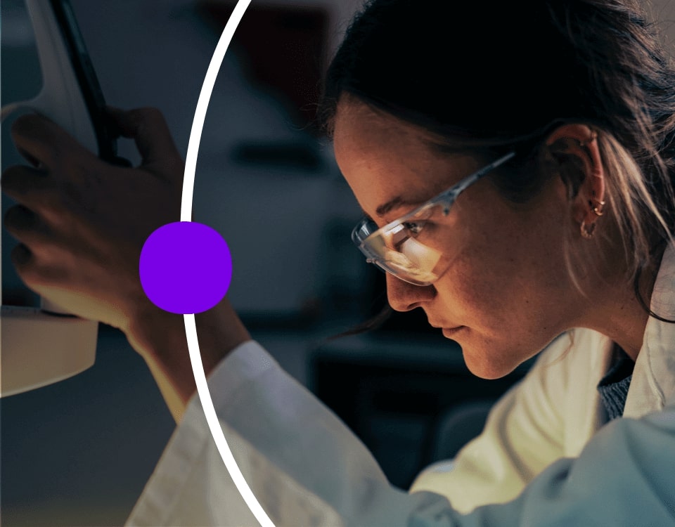 Woman in lab coat and safety glasses using laboratory instrument