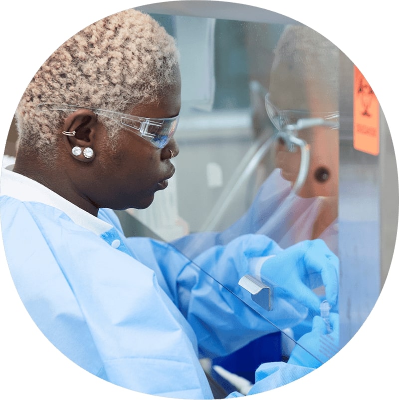 Femme portant une blouse de laboratoire et des lunettes de sécurité travaillant avec des matériaux de laboratoire sous verre