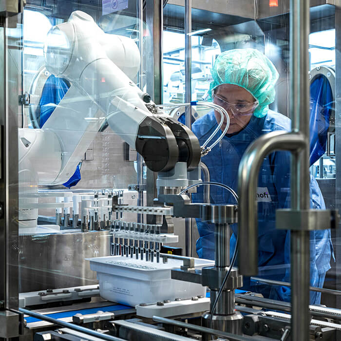 Personne en blouse de laboratoire et lunettes de sécurité, tenant un flacon pour le regarder