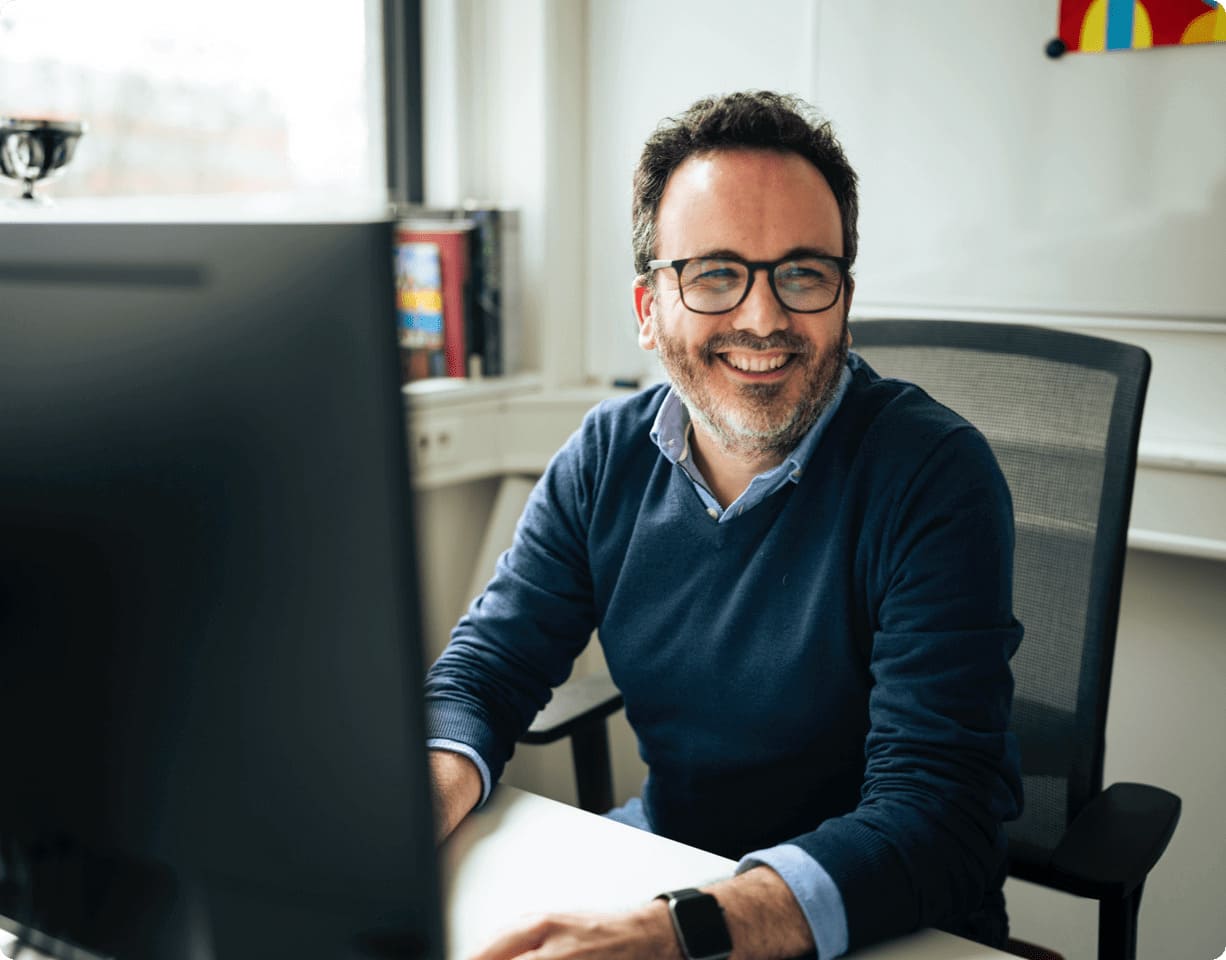 homme souriant assis au bureau avec un ordinateur