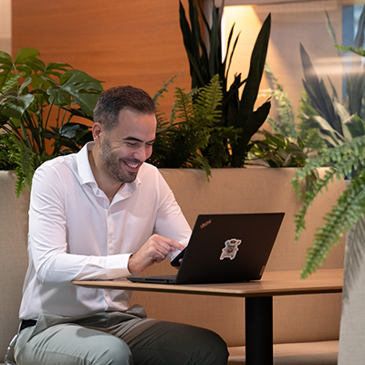 Man smiling while working on laptop in lounge.