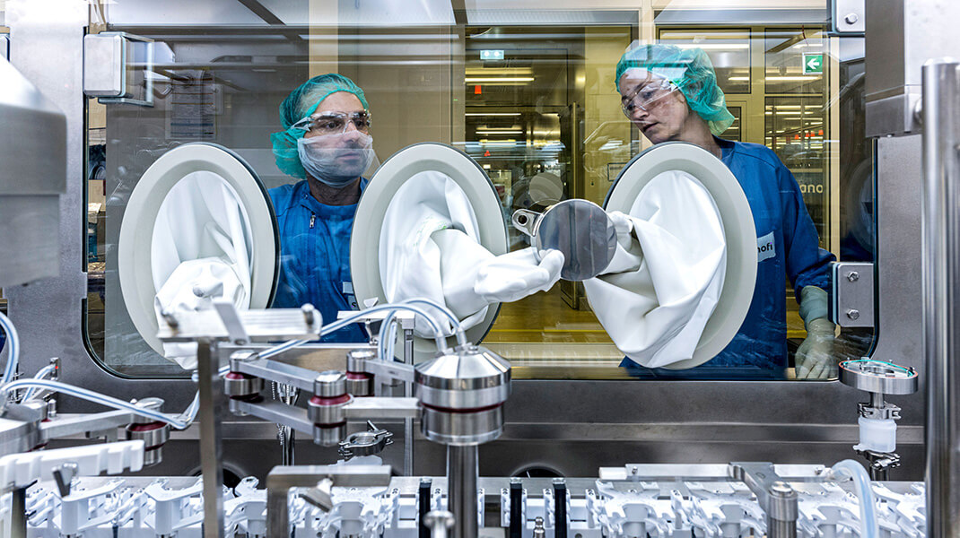 Des employés de laboratoire en tenue stérile travaillent avec des échantillons sous verre