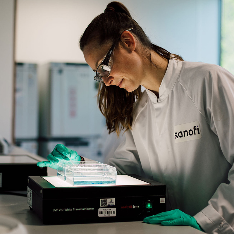Scientist in a lab coat examines a sample under UV light in a modern laboratory environment.