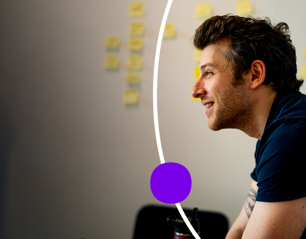 Man smiling in a meeting with sticky notes on the wall.