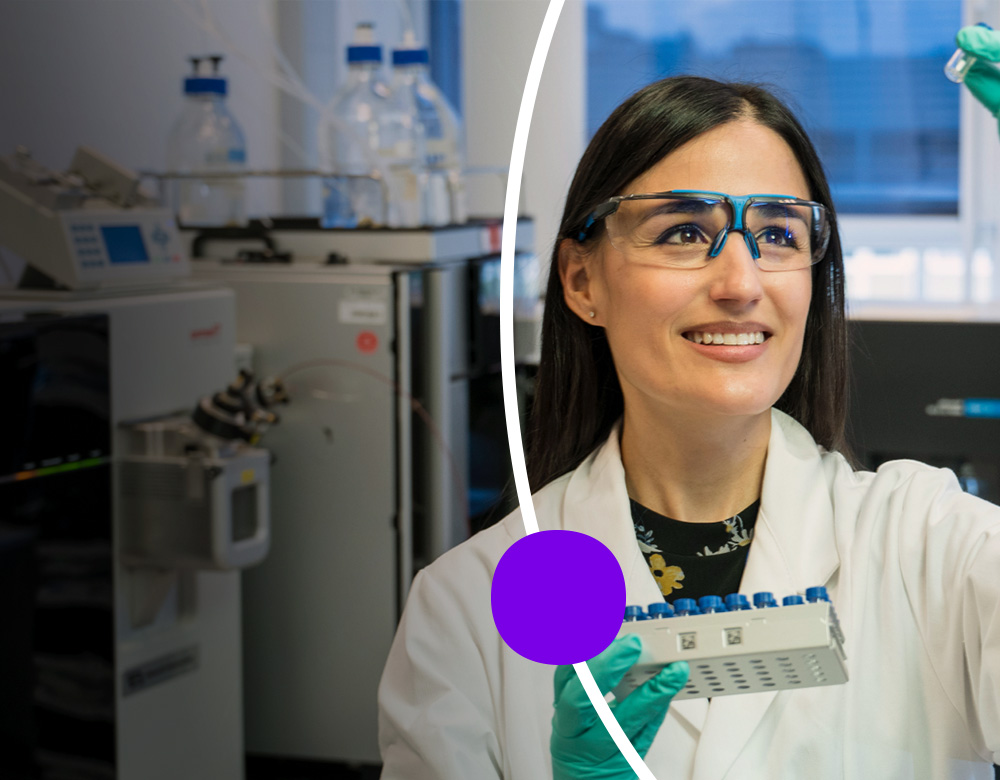 A woman in a lab coat holds a lab tubes and smiling confidently.