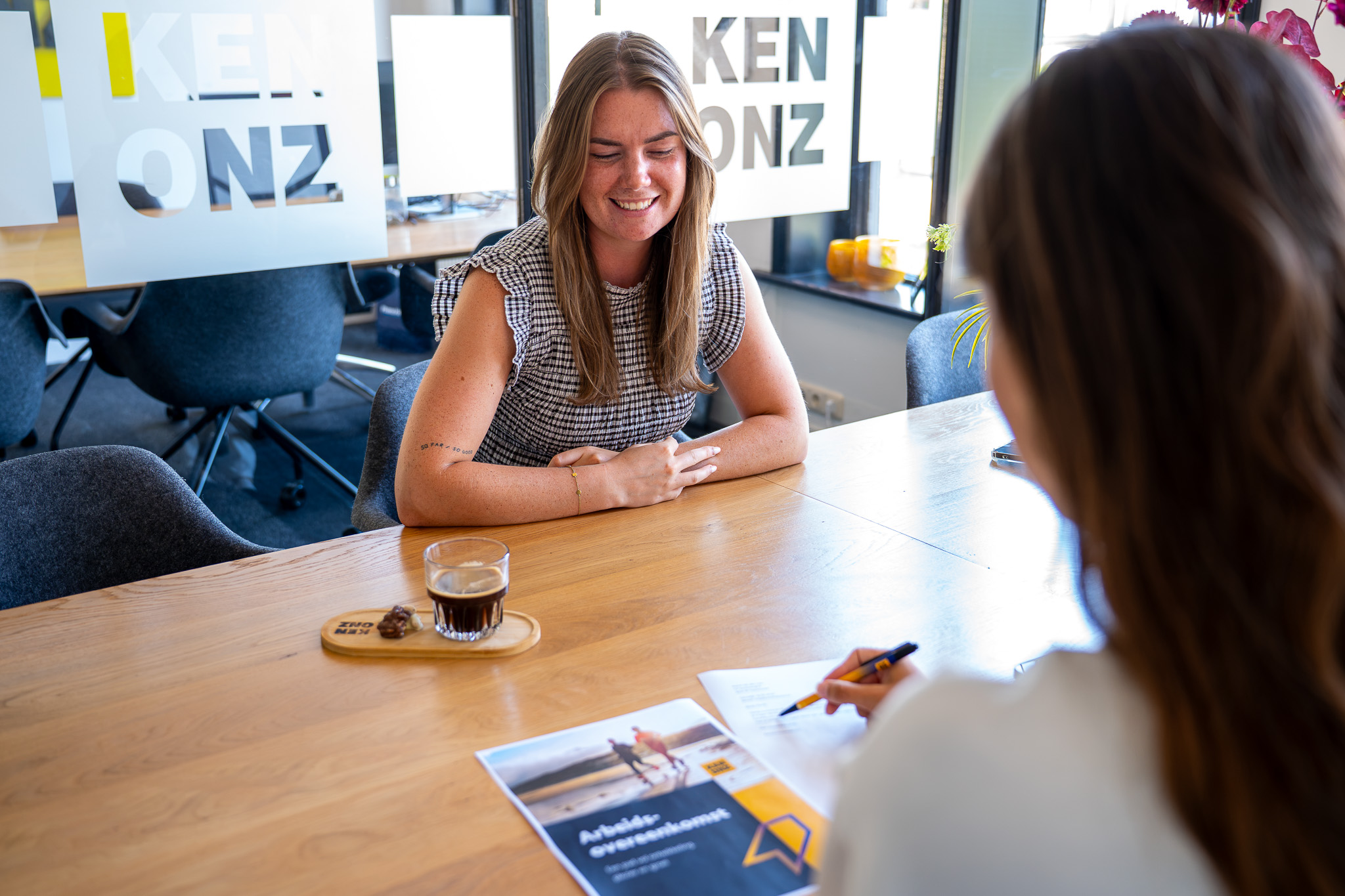 Collega's tegen over elkaar aan tafel in gesprek over arbeidsovereenkomst bij Kenonz.